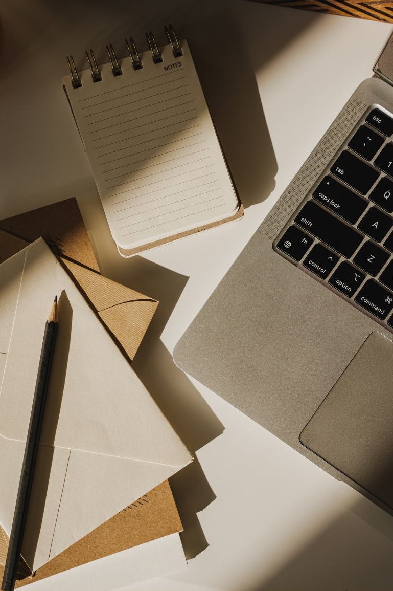 Caderno, envelopes e lápis sobre a mesa ao lado de um notebook
